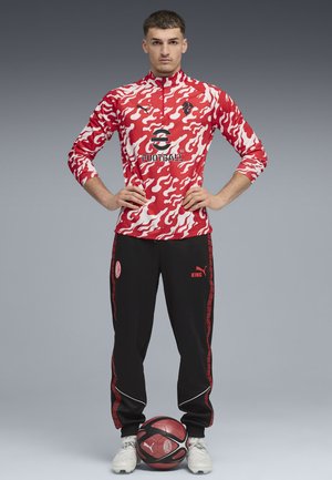 Rød og hvid camo langærmet trøje med sorte bukser, der har røde detaljer. Inkluderer logo designs og en fodbold ved modellens fødder.