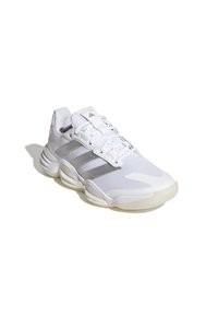 Chaussure de sport blanche avec tige en maille, trois rayures grises, languette rembourrée et semelle texturée. Dispose d'un système de laçage et d'un design de bout arrondi.