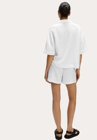 Camicia bianca a maniche corte con texture abbinata a pantaloni corti bianchi. L'outfit presenta una vestibilità comoda ed è completato da sandali neri.
