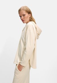 Beige hooded sweatshirt with a relaxed fit, made of soft fabric, featuring a front pocket and ribbed cuffs, paired with matching pants.