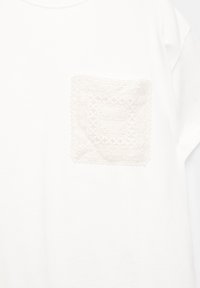 Witte T-shirt met een gekleurde, geborduurde zak in een lichte beige kleur, met ingewikkelde patronen en kantige randen.