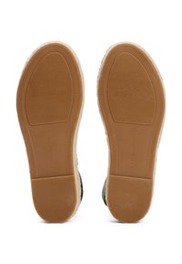 Semelles de chaussures noires avec caoutchouc texturé et bord beige clair. Présentent des motifs lisses et nervurés, étiquetées "TOMMY HILFIGER" au bas.