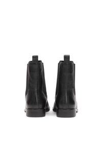 Botas de tobillo de cuero negro con textura suave, paneles laterales elásticos y un tacón bajo cuadrado, con un diseño minimalista y sin marcas visibles.