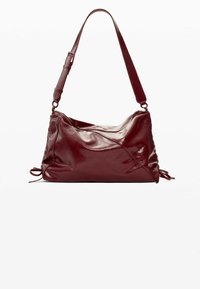 Bolso de hombro de cuero burdeos con textura suave, forma blanda, correa ajustable y detalle de cordón en los laterales.