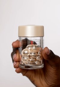 Transparent glasburk med ett guldock som innehåller ljuskrämiga ceramidkapslar. Etiketten säger "Hyaluronsyror Hydra-Plumpande Serum."