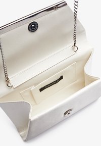 Bílá perleťová kabelka na ples s stříbrným řetízkovým popruhem, zapínáním na patentku a hladkým vnitřkem s kapsou s logem značky.