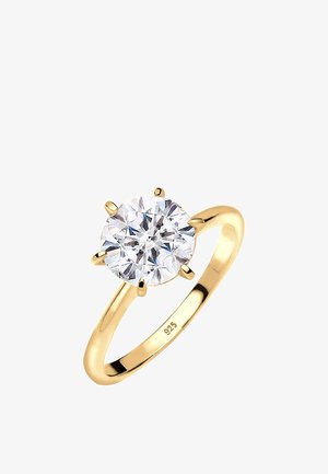 Anillo chapado en oro con una gran piedra redonda y clara en un engaste de seis garras. La banda es lisa y presenta un acabado pulido. Marcado "925."