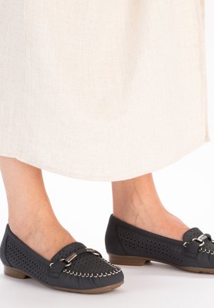 Black perforated loafers with a flat brown sole, featuring decorative stitching and a silver buckle accent. Textured upper material.