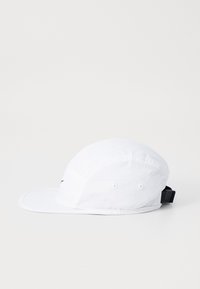 Hvitt caps med buet skygge, laget av lett stoff. Har ventilasjons hull og en justerbar sort stropp bak.