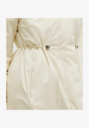 Artimos plano smėlio spalvos švarko juosmuo su reguliuojamu raišteliu ir sidabriniu ryšiu, matyti sklandus audinys ir šoninės kišenės siūlė.