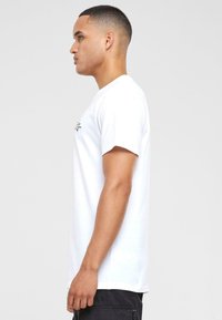 White cotton t-shirt with short sleeves, relaxed fit, and a small black graphic on the chest. Smooth texture and standard crew neck design.