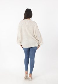 Maglione oversized color beige chiaro con maniche ampie, abbinato a jeans blu aderenti e sandali con tacco trasparente. Tessuto a maglia semplice e con texture.