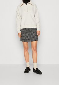 Krémový fleece pulovr se zipem u límce. V kombinaci s mini sukní s černobílým vzorem. Černé mokasíny a světlé ponožky dotvářejí celý vzhled.
