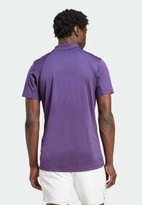 Lila Polo-Shirt mit kurzen Ärmeln, strukturiertem Kragen, glatter Textur und kontrastierenden Nähten an den Schultern, kombiniert mit weißen Shorts.