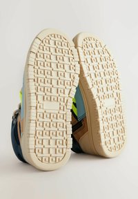 Flerfärgade sneakers med en strukturerad krämfärgad gummisula. Funktioner inkluderar blå, gula och bruna material samt ett zigzag-mönster på sålen.