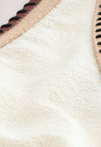 Gros plan d'un tissu éponge blanc doux avec des bords tricotés beige et noirs.