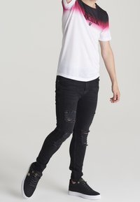 Jeans rotos negros combinados con una camiseta degradada que pasa de rosa a blanco, con un logo negro en la parte delantera y mangas cortas.