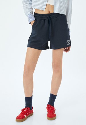 Mørkeblå bomuldsshorts med elastisk talje og snor. Har sidelommer og hvid logo-print på nederste venstre front.