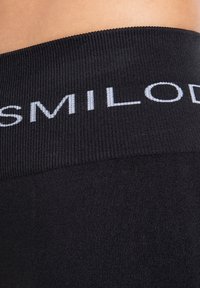 Närbild av ett svart elastiskt midjeband på kläder med delvis vit text "SMILOD" på ribbat tyg.