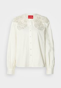 Biela košeľa na gombíky s dekoratívnym vyšívaným čipkovým golierom. Má dlhé rukávy s nariasenými manžetami a pohodlný strih.