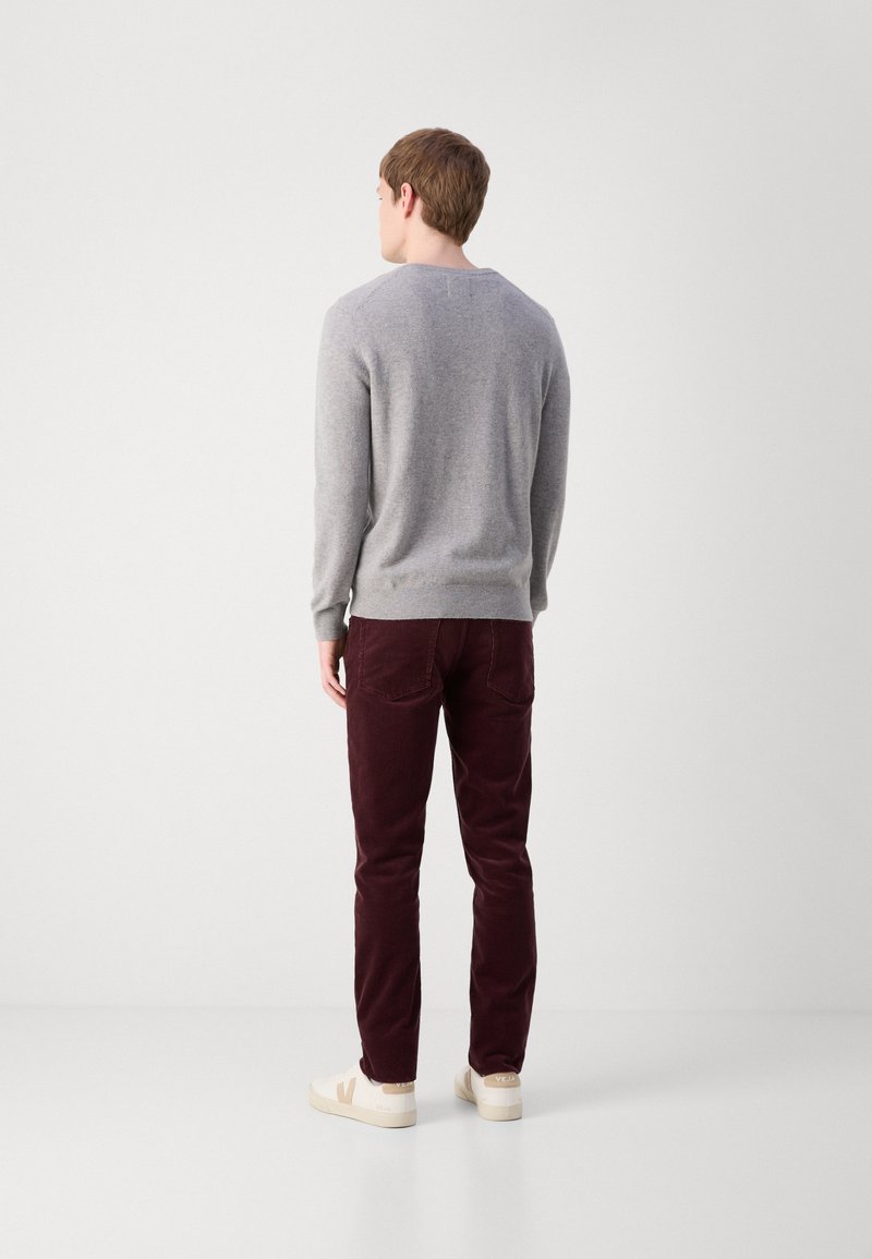 Grauer Strickpullover, kastanienbraune Cordhosen und cremefarbene Sneaker. Der Pullover hat einen runden Hals und gerippte Bündchen, sichtbare Nähte und Taschen.