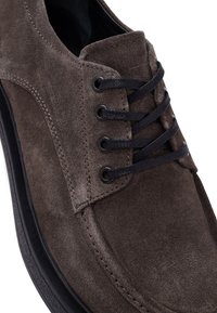 Brown suede lace-up shoe with black laces, round toe, and textured surface; features black rubber sole and eyelets for laces.