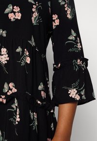 Vestido negro con un patrón floral de flores rosas y hojas verdes. Mangas acampanadas con acentos de volantes y un diseño de capas.