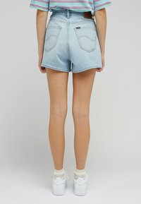 Jasnoniebieskie szorty dżinsowe z wysokim stanem, lekko zaokrąglonym dołem i dwiema tylnymi kieszeniami, w połączeniu z białymi trampkami i kremowymi skarpetkami.