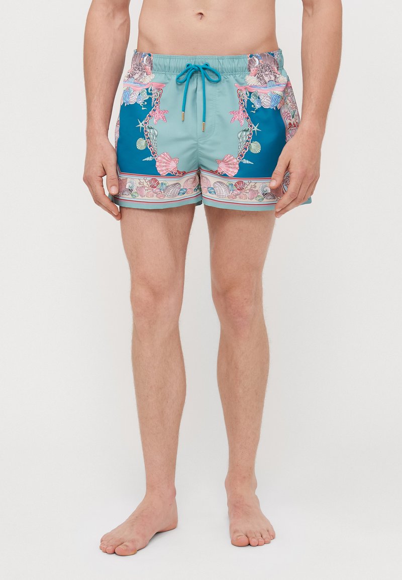 Σορτς κολύμβησης σε τιρκουάζ και μπλε χρώμα με σχέδιο από κογχύλια, ελαστική ζώνη και κορδόνι. Το υλικό φαίνεται ελαφρύ και στεγνώνει γρήγορα.