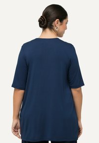 Tmavě modrý krátký rukáv top, vyrobený z měkké látky. Má volný střih, kulatý výstřih a minimalní švy na zadní straně.