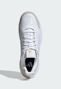 Baskets blanches avec une tige en cuir lisse perforé, des accents beiges, des lacets plats et un logo de semelle intérieure noir et blanc.