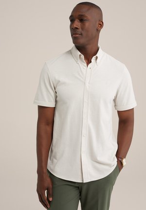 Camisa de manga corta abotonada en algodón beige claro. Presenta un cuello clásico, puños enrollados y un discreto detalle del logo en el pecho.