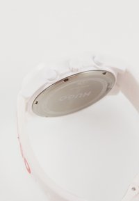 White watch with a silicone strap and metal back. Features two buttons on the side and a subtle logo near the strap. Smooth, matte finish.