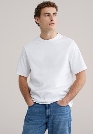 Witte katoenen T-shirt met korte mouwen, een ronde hals, een losse pasvorm en een gladde textuur, gecombineerd met lichtblauwe spijkerbroek.