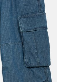 Μπλε τζιν cargo παντελόνι με κάθετες ρίγες, που διαθέτει μπαλώματα τσέπες στα πλάγια και χαλαρή εφαρμογή. Αυτή είναι κατασκευασμένη από μαλακό υλικό με ανεπίσημο σχέδιο.