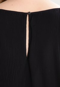 Närbild av bakre halsringning med en liten ögla-och-knapp stängning på svart vertikalt ribbat tyg.