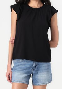 Mustat lyhythihaiset puserot, joissa on röyhelökoristeet, valmistettu pehmeästä kankaasta. Yhdistetty vaaleansinisiin farkkushortseihin, joissa on rento istuvuus.