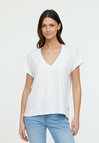 T-shirt blanc à col en v avec des manches courtes retroussées, fabriqué en tissu doux, offrant une coupe décontractée et un petit détail logo sur l'ourlet.