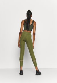 Leggings atletici verde oliva con vita alta e dettagli in rete trasparente. Abbinati a un crop top a coste coordinato e sneakers nere.