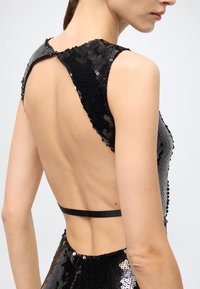 Black sequined dress with a deep back cut, featuring a black satin strap. Smooth texture with shiny sequins creating a reflective surface.