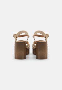 Beige suède hoge hakken sandalen met een brede bruine houten blokhak en verstelbare enkelbandjes, voorzien van een gladde textuur en eenvoudig ontwerp.