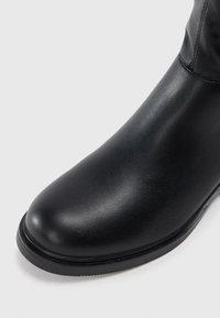 Botín de cuero negro hasta el tobillo con punta redonda, textura suave y costuras acolchadas. Suela de goma de perfil bajo con un patrón de tracción discreto.