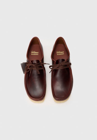 Zapatos de cuero marrón con punta redondeada, diseño con cordones y suela de goma color beige. Presentan una costura y plantilla con marca.