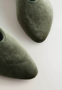 Flade sko i velourgrøn med en spidse tæer-design, elastisk kant øverst og en glat overflade. Sålen er sort med en let krumning ved tåen.