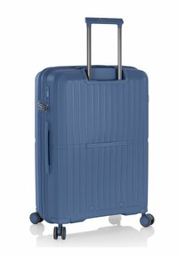 Valigia rigida blu con texture scanalata, manico retraibile e quattro ruote per la mobilità. Presenta una cerniera e un manico laterale.