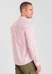 Chemise à manches longues en tissu rose clair avec un motif floral, col boutonné, et manches à poignets, présentant un ourlet droit et une coupe décontractée.
