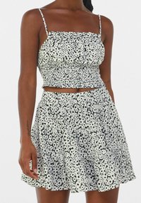 Schwarzes und weißes florales Croptop mit gerafftem Design, ergänzt durch einen passenden schwingenden Rock, beide mit einem rüschenbesetzten Saum.