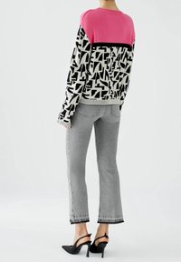 Pull en maille avec une partie supérieure rose, motif abstrait noir et blanc en dessous. Associé à un jean gris et des chaussures à talons noirs.