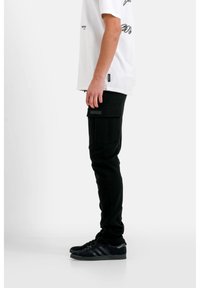 Zwarte cargo broeken met een slim fit, voorzien van zijzakken en een textuurstof. Gecombineerd met zwarte sneakers. Het model draagt een kort wit T-shirt.