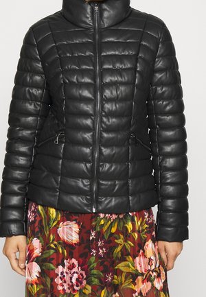 Schwarze gesteppte Lederjacke mit Frontreißverschluss, getragen über einem roten und rosa gemusterten Rock mit Blumenmuster, dargestellt von den Schultern bis zur Hüfte.